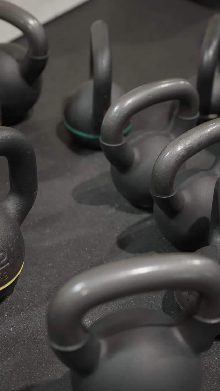 vertical - Close up of black kettlebells with colored weight markings placed on rubber gym floor indoors