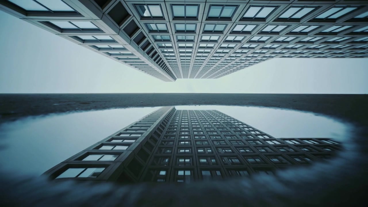 Initial ripple appearing in shallow puddle, tall office building reflecting and warping window grid