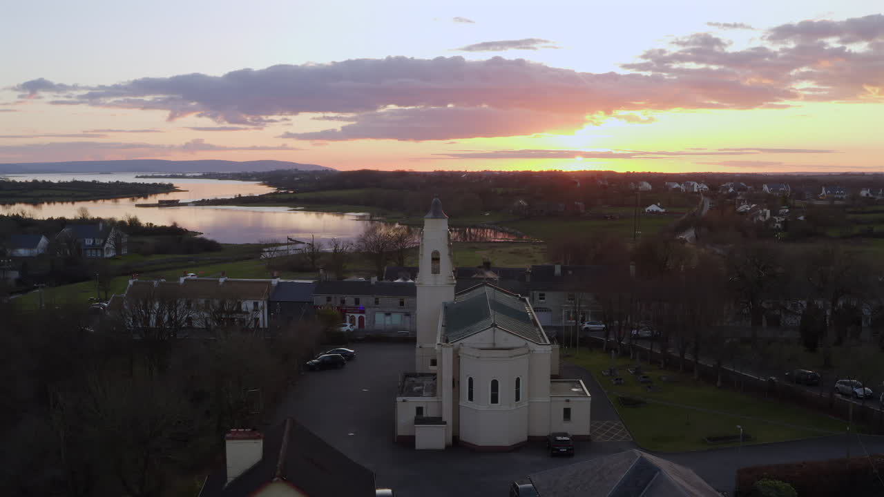 Slow motion river at sunset with glowing reflections as cars drive in front of church, Clarinbridge, Ireland