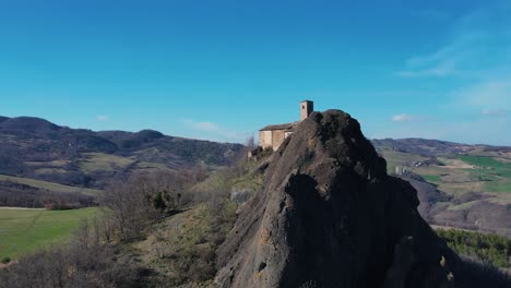 aerial footage of pietra perduca, volcanic rock, church set at top stone immersed in countryside landscape, cultivated land in val trebbia bobbio, emilia romagna, italy