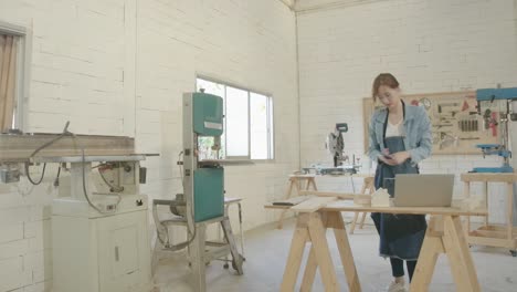 4k hyper-lapse of young asian woman carpenter building design house model with laptop computer, zoom in.  cutting and drilling wooden working in workshop office studio, personal business concept.