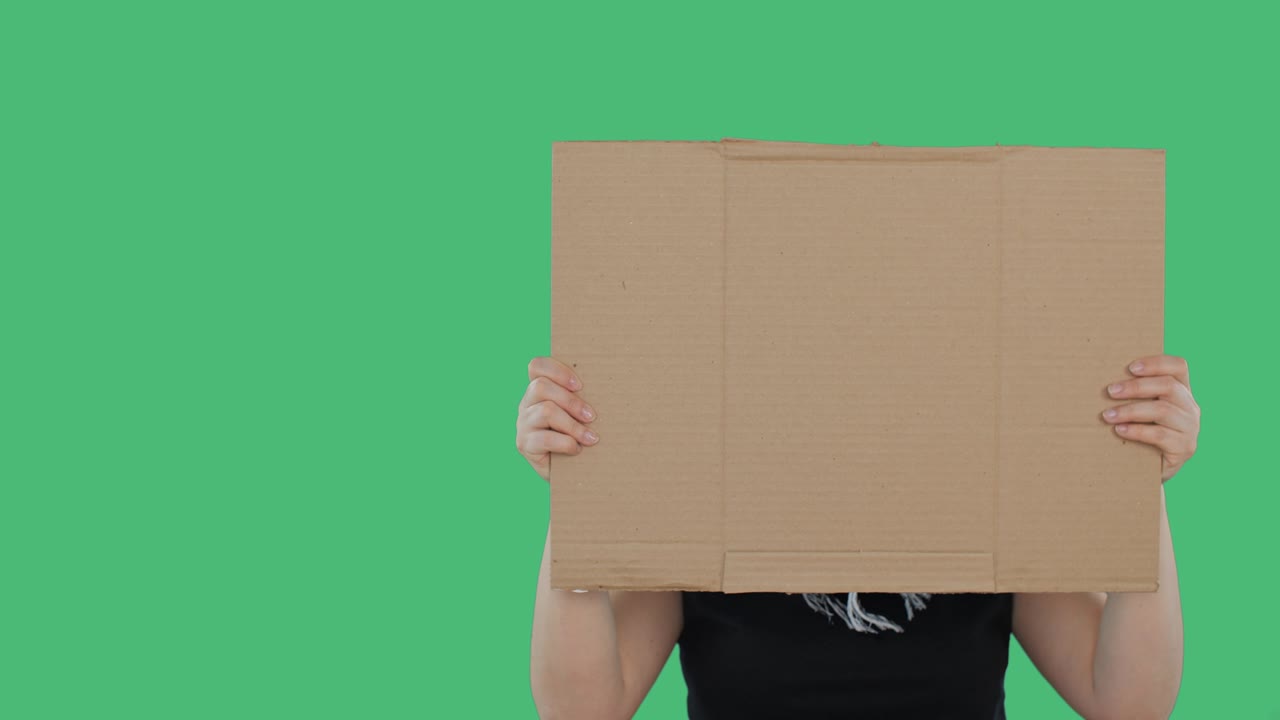 Female hands holding empty cardboard on green background. Unrecognizable woman showing cardboard banner on strike at empty green screen.
