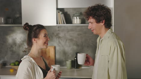 couple talking and drinking from mugs in the kitchen