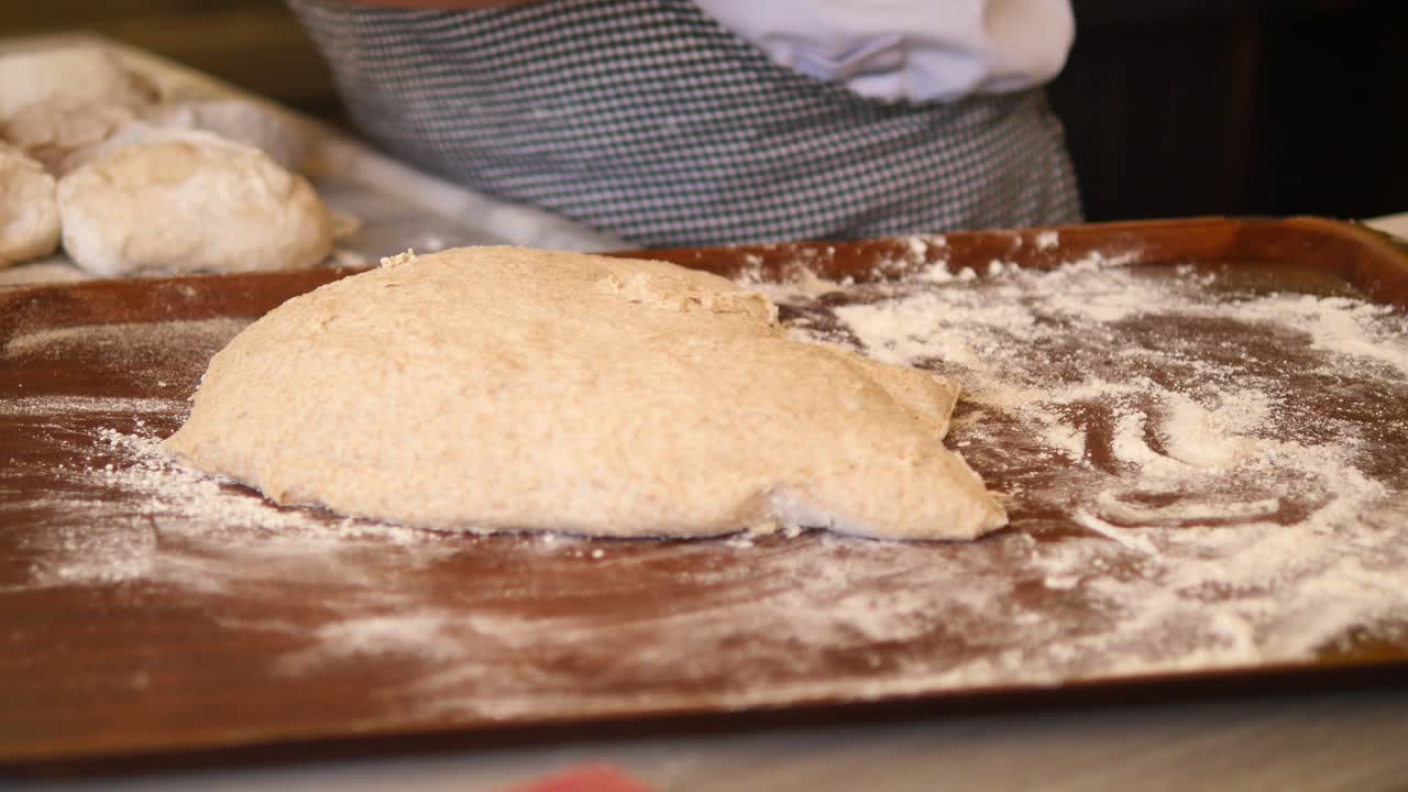 Baker kneading bread dough on a tray