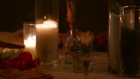 wedding party banquet outdoors in forest. dining table decorated in boho style with burning candles, white cloth, flowers, served with plates, tableware, dishes, meals, stemware and drinks at night