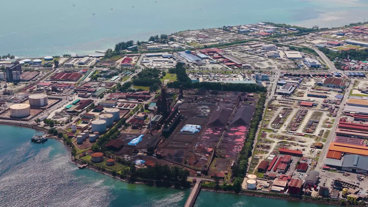 Aerial view of the Rancha-Rancha Industrial Estate in Labuan, Malaysia, showcasing a steel mill and sponge iron plant near the coastline under bright daylight