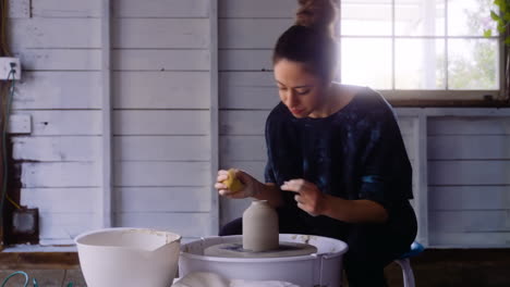 potter puts finishing touches on clay vase on pottery wheel in her workshop