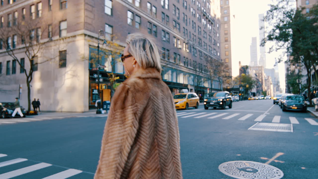 New York, USA, 2 April 2026: Portrait of woman in fur coat on New York City street crossing. Mid shot of blonde woman looking at camera wearing sunglasses and fur coat with urban traffic in background