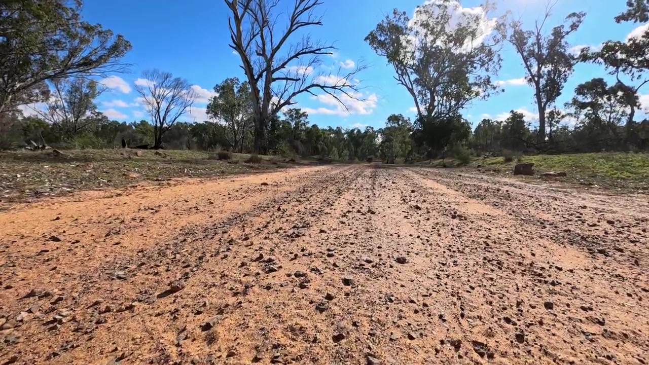 Static low angle shot of a red gravel road through arid scrubland in Australia.