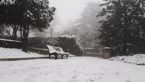 Snowfall-on-a-park-with-a-bench-and-surrounded-by-trees-during-winter-in-the-Mtatsminda-Park,-Tbilisi,-Georgia