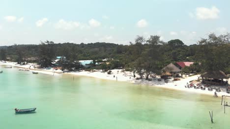 Agua-Clara-Paradisíaca-Llena-De-Barcos-De-Pesca-Que-Bañan-La-Arena-Dorada-En-La-Playa-De-Sok-San-En-Koh-Rong-Sanloem,-Camboya---Tiro-Aéreo