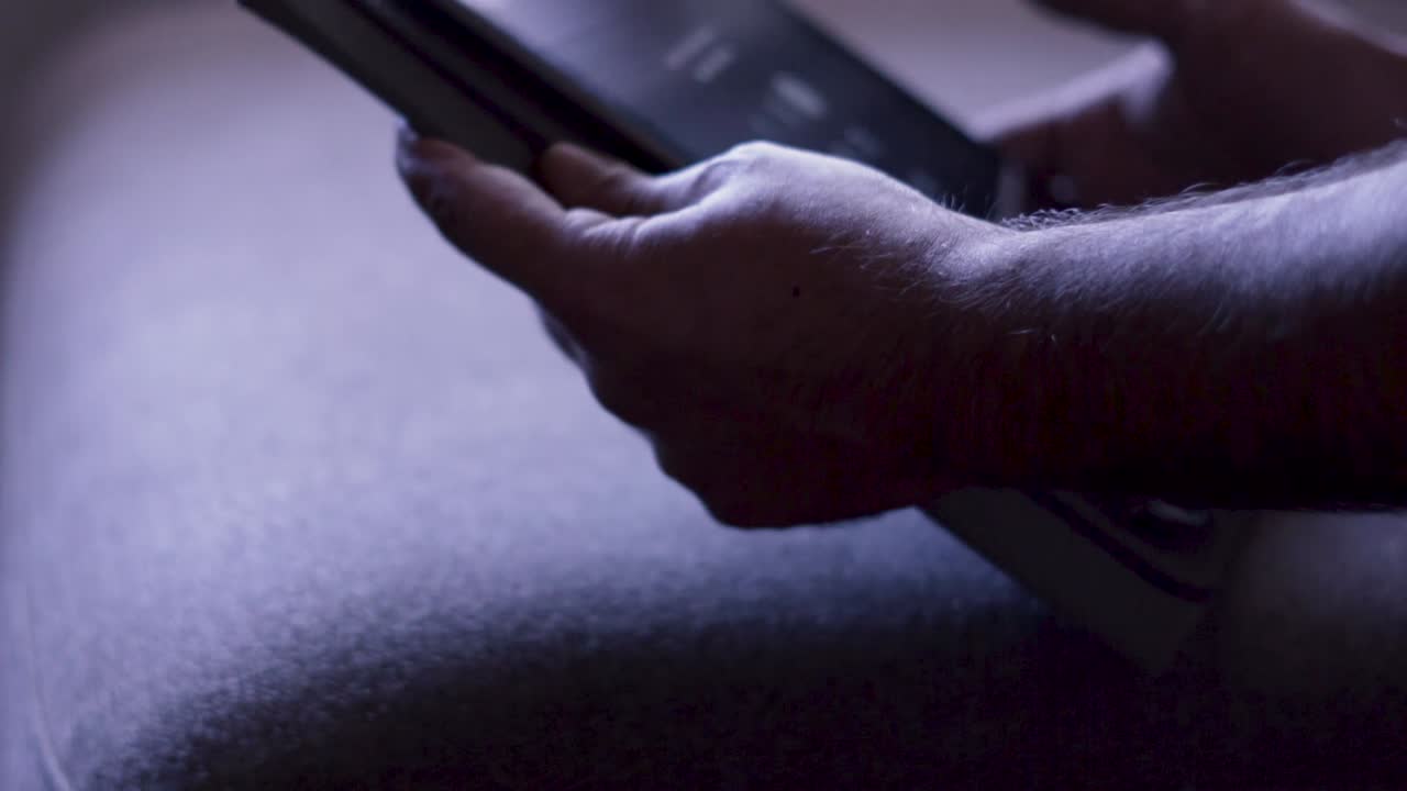 Shooted in slow motion showing man's hands browsing social media or playing with a mobile tablet at evening (dark space)