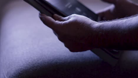 shooted in slow motion showing man's hands browsing social media or playing with a mobile tablet at evening (dark space)