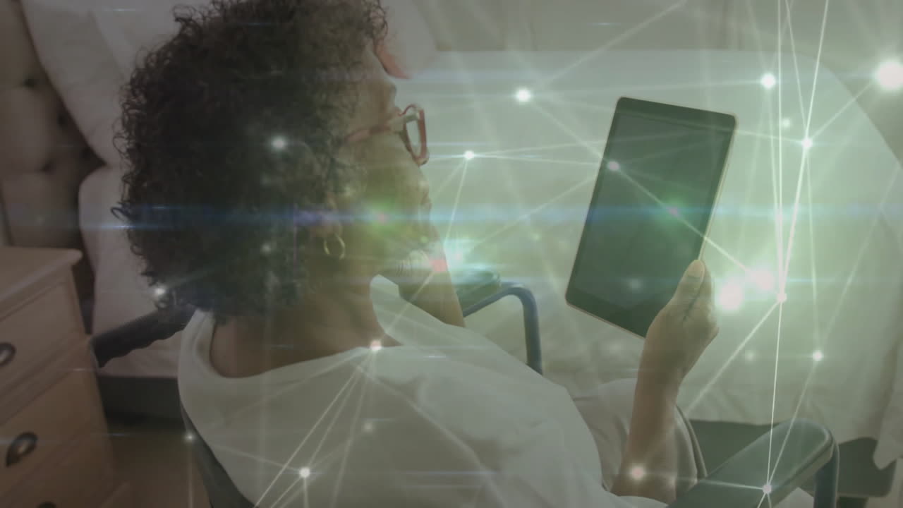 senior woman in wheelchair holding tablet at bedside, showing health tech graphs and digital links