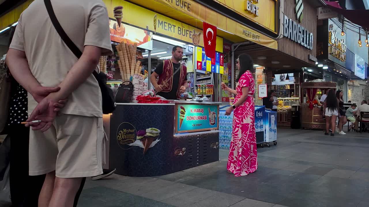 Immerse yourself in the bustling atmosphere of a lively street in Konya, Turkey as a gelato vendor captivates customers with their skilled gelato preparation and entertaining tricks