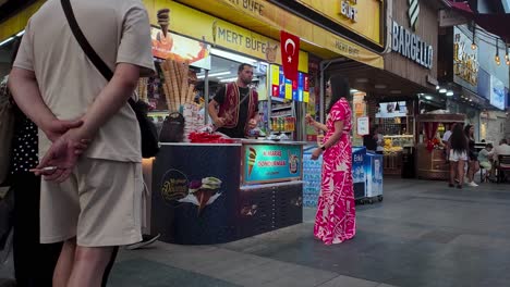 immerse yourself in the bustling atmosphere of a lively street in konya, turkey as a gelato vendor captivates customers with their skilled gelato preparation and entertaining tricks