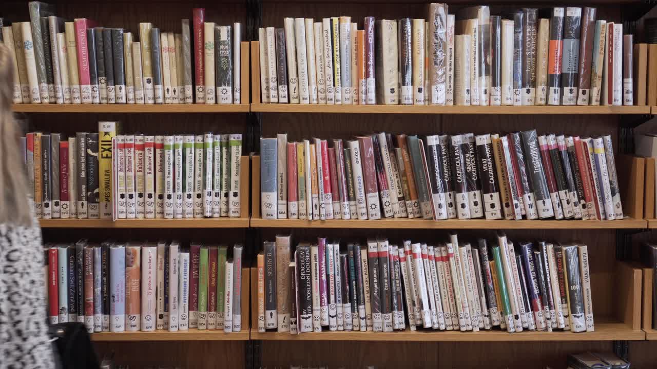 Young female is choosing a book from bookshelf and walking off a screen
