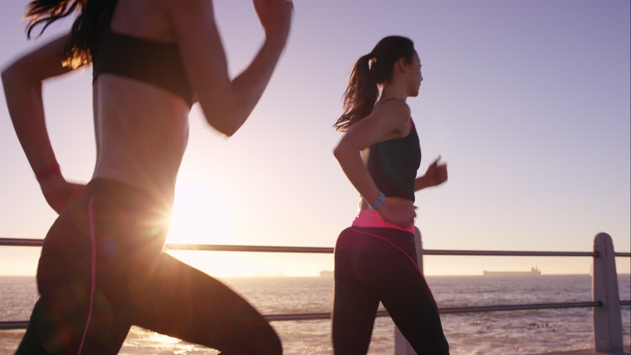 Two athletic woman running outdoors slow motion on promenade at sunset near ocean enjoying evening run