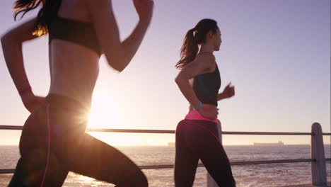 Two-athletic-woman-running-outdoors-slow-motion-on-promenade-at-sunset-near-ocean-enjoying-evening-run