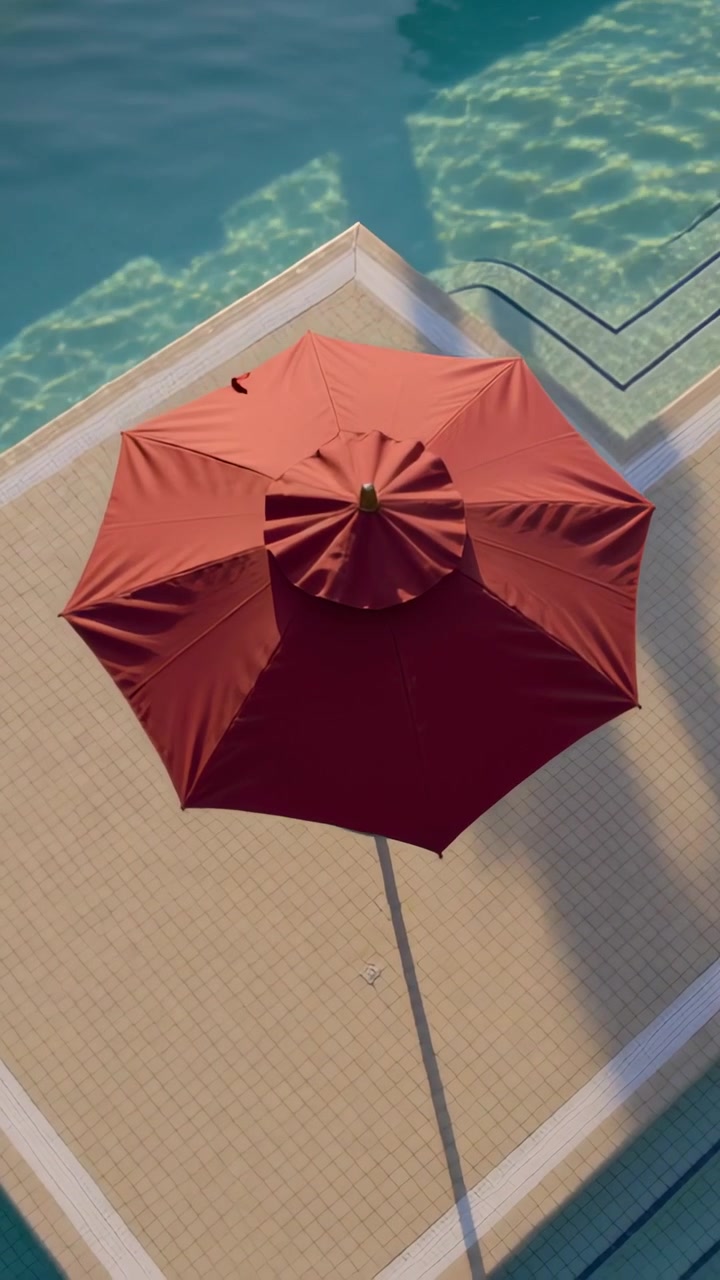Vertical video: Panning drone centering red umbrella on tiled pool deck, revealing leaf and steps