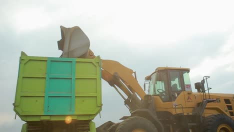 west java indonesia - february 11, 2002 : heavy construction machinery excavator in open pit mining - wheel loader transporting sand to truck or trailer in asphalt plant.