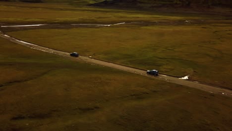 aerial view over two cars speeding on a dirt road through icelandic highlands