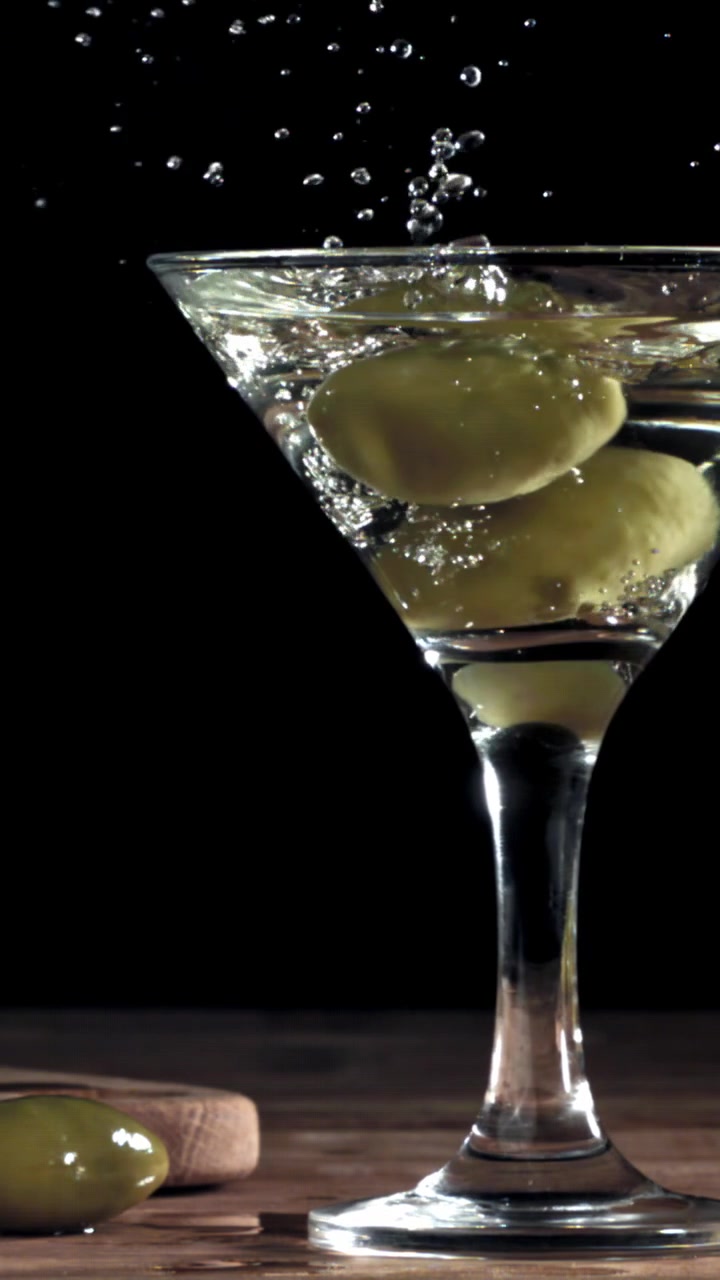 Aceitunas verdes salpicando en una copa de Martini en cámara lenta