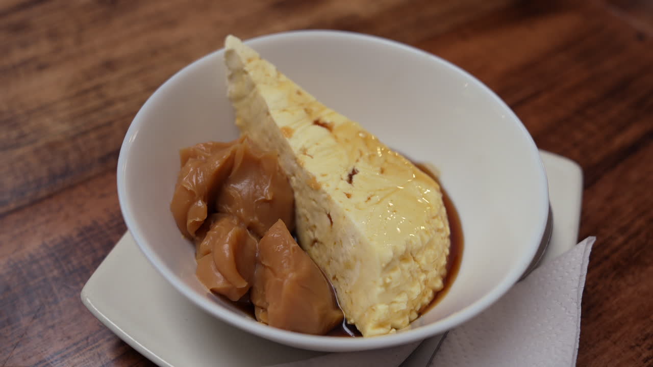 Indulging close-up of a creamy cheesecake paired with caramel sauce, elegantly served on a rustic wooden table, capturing a warm, inviting culinary scene