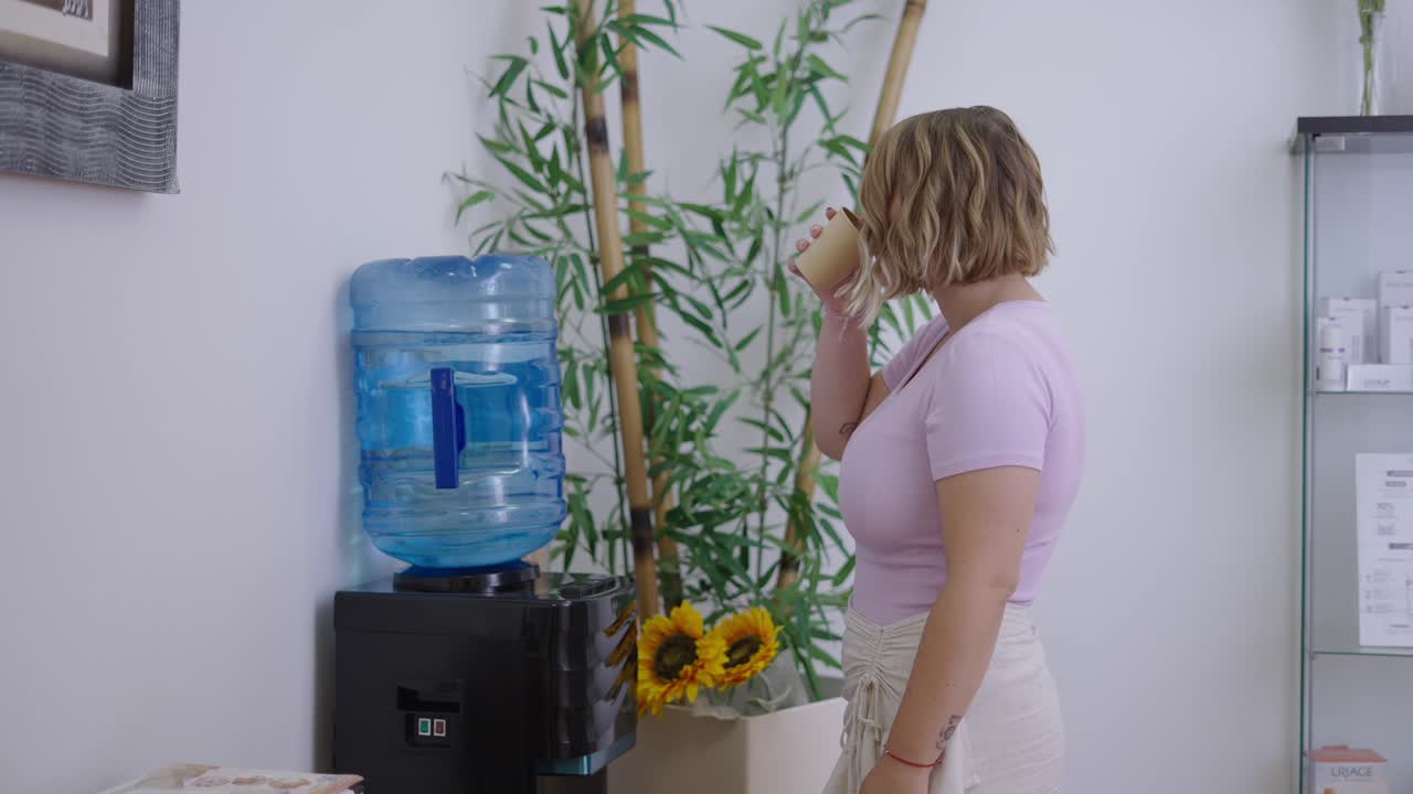 Woman gets water from a water cooler in an office or waiting room