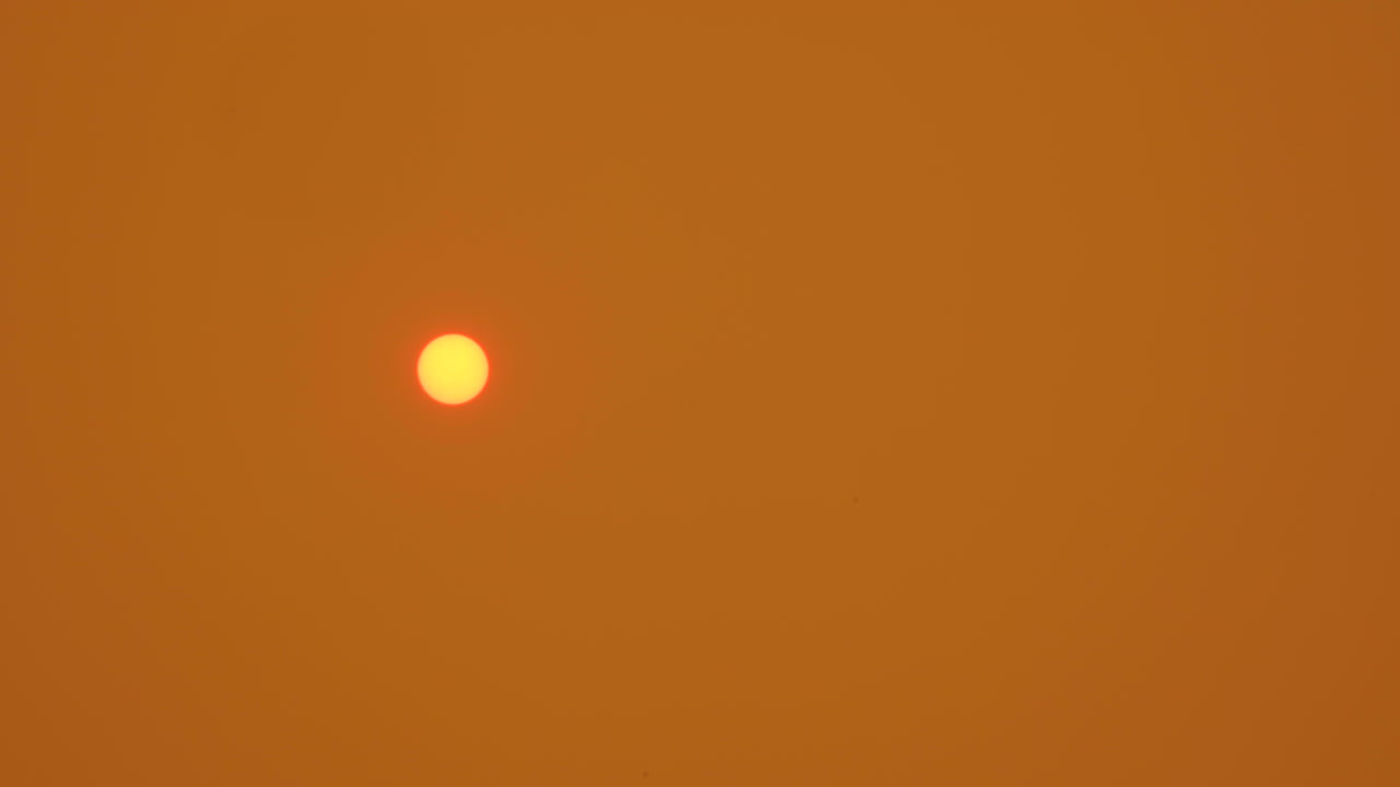 sol naranja en el cielo naranja ahumado mientras la ceniza se deposita en la lente