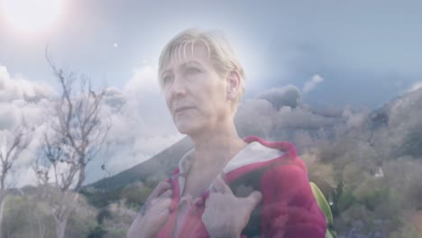 happy caucasian senior woman hiking in mountains over fast moving clouds