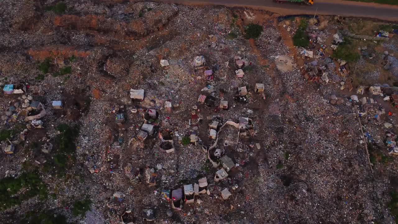 Aerial view of a large open landfill next to a expressway in rural Nigeria, Africa. The drone tilts down and garbage pickers can be seen at work and sorting the trash