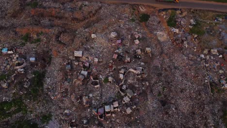 aerial view of a large open landfill next to a expressway in rural nigeria, africa. the drone tilts down and garbage pickers can be seen at work and sorting the trash