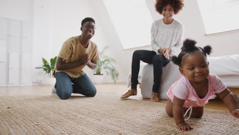 Niña-Aprendiendo-A-Gatear-En-Casa-Mientras-Los-Padres-Se-Sientan-En-El-Suelo-Y-La-Alientan