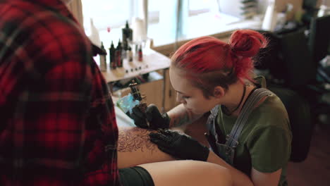 tattoo artist working on client's leg