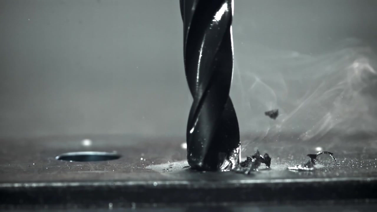 Close-up of a drill bit drilling into metal with smoke