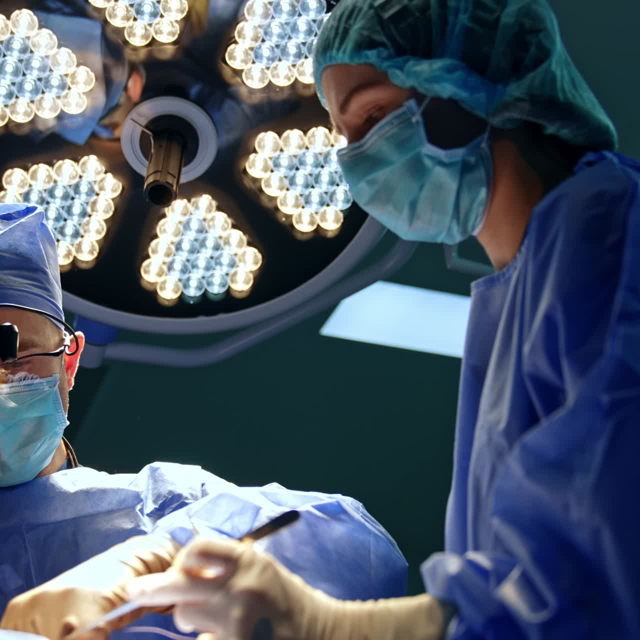 Male neurosurgeon in device glasses performs surgery. Female nurse preparing tools for the doctor. Low angle view