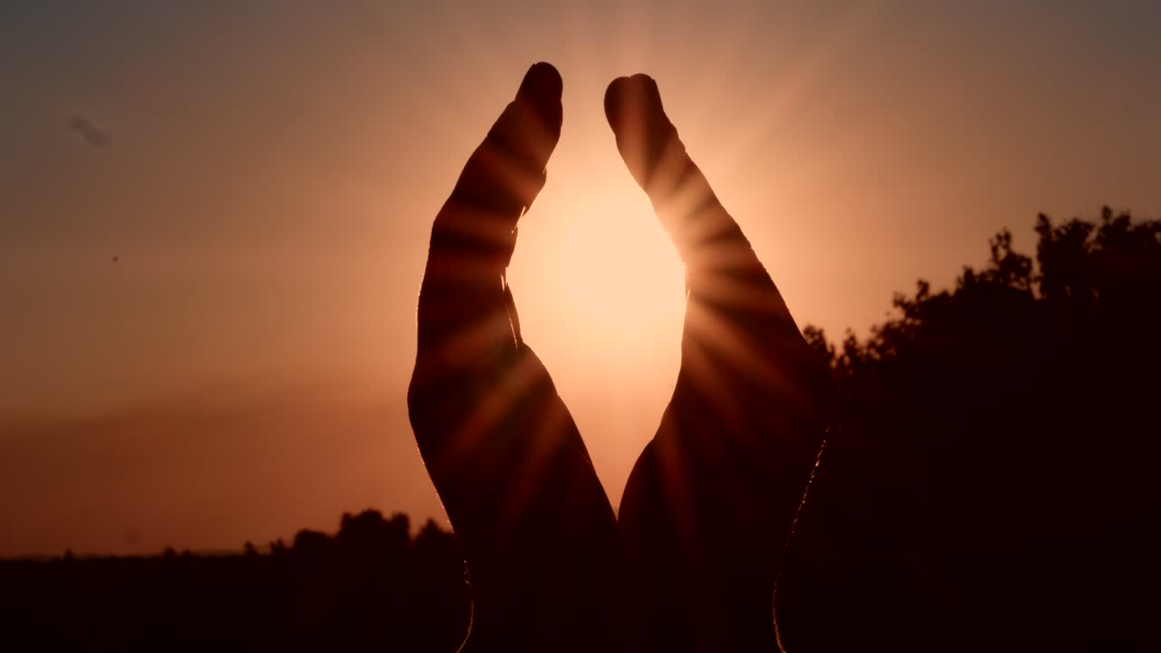 Sagoma di mani che racchiudono il sole al tramonto