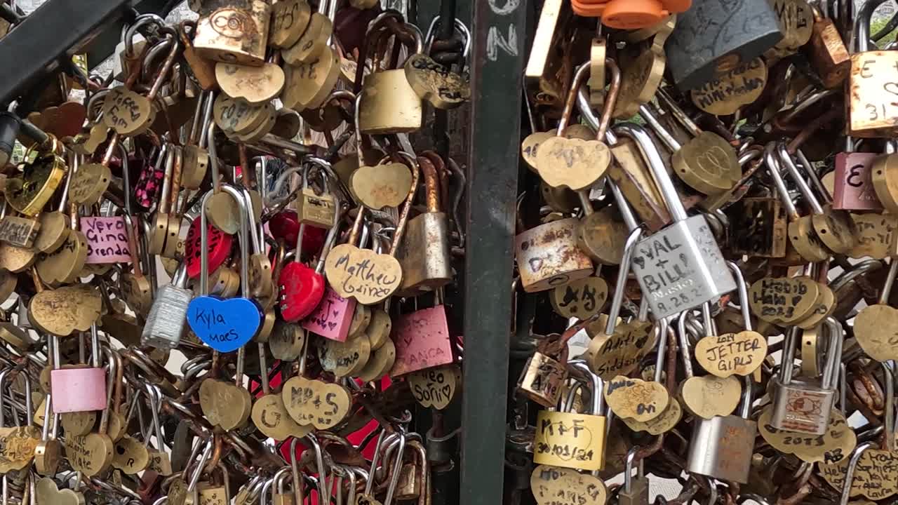 A dense collection of heart-shaped padlocks with engraved messages on a metal fence.