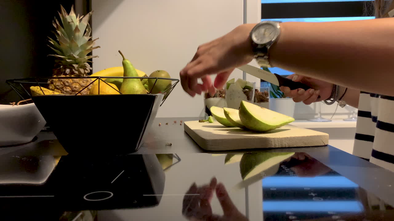mujer atractiva en la cocina preparando un postre fresco con pera, chica cortando una pera verde en una tabla de madera