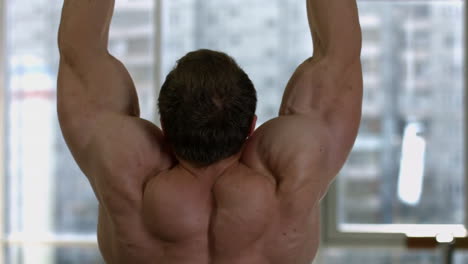 Back-of-a-muscular-man-with-strong-muscles-doing-hanging-pull-ups,-shirtless-bodybuilder-exercising