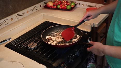 mujer salteando champiñones maitake con mantequilla burbujeante en una sartén en una pequeña cocina casera