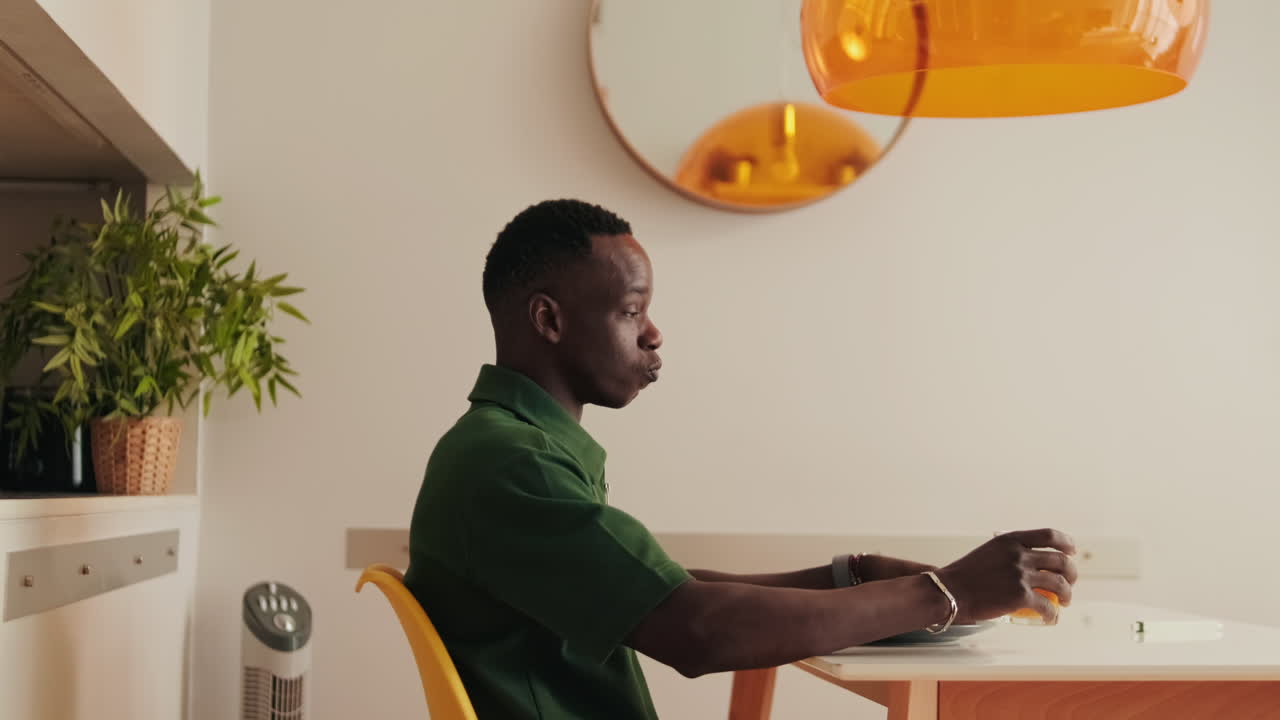 African American Man Drinking Juice and Preparing Sandwich at Home