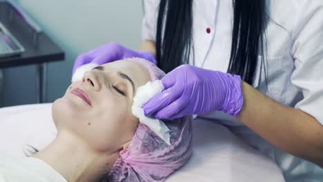 hands in blue gloves of experienced cosmetician cleaning female's face with sterile napkins. young woman is receiving treatments in beauty salon.
