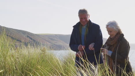 loving active senior couple hugging as they walk along coastal path against flaring sun