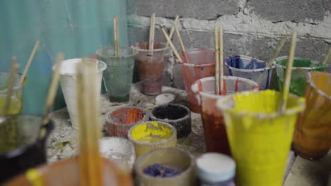 number of colorful paint brushes and containers at an indoor custom surfboard making workshop lying at a corner