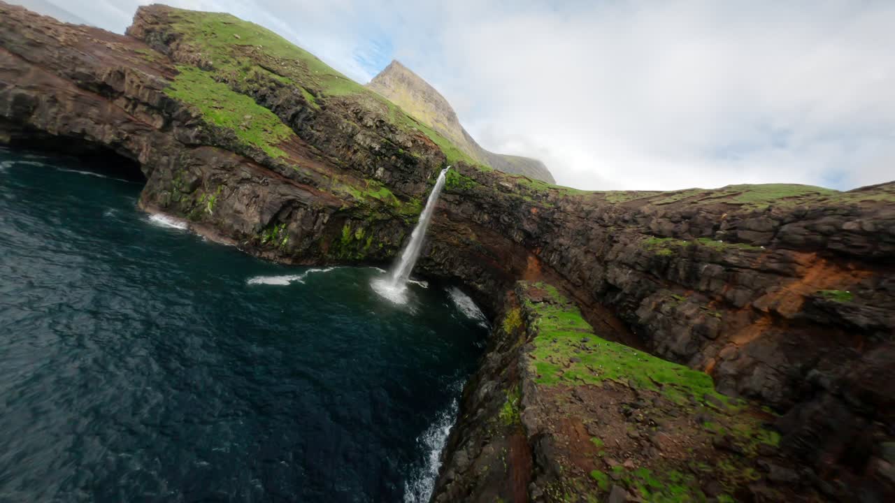 una serena cascada se sumerge en el océano cerca de la aldea de gásadalur, islas feroe