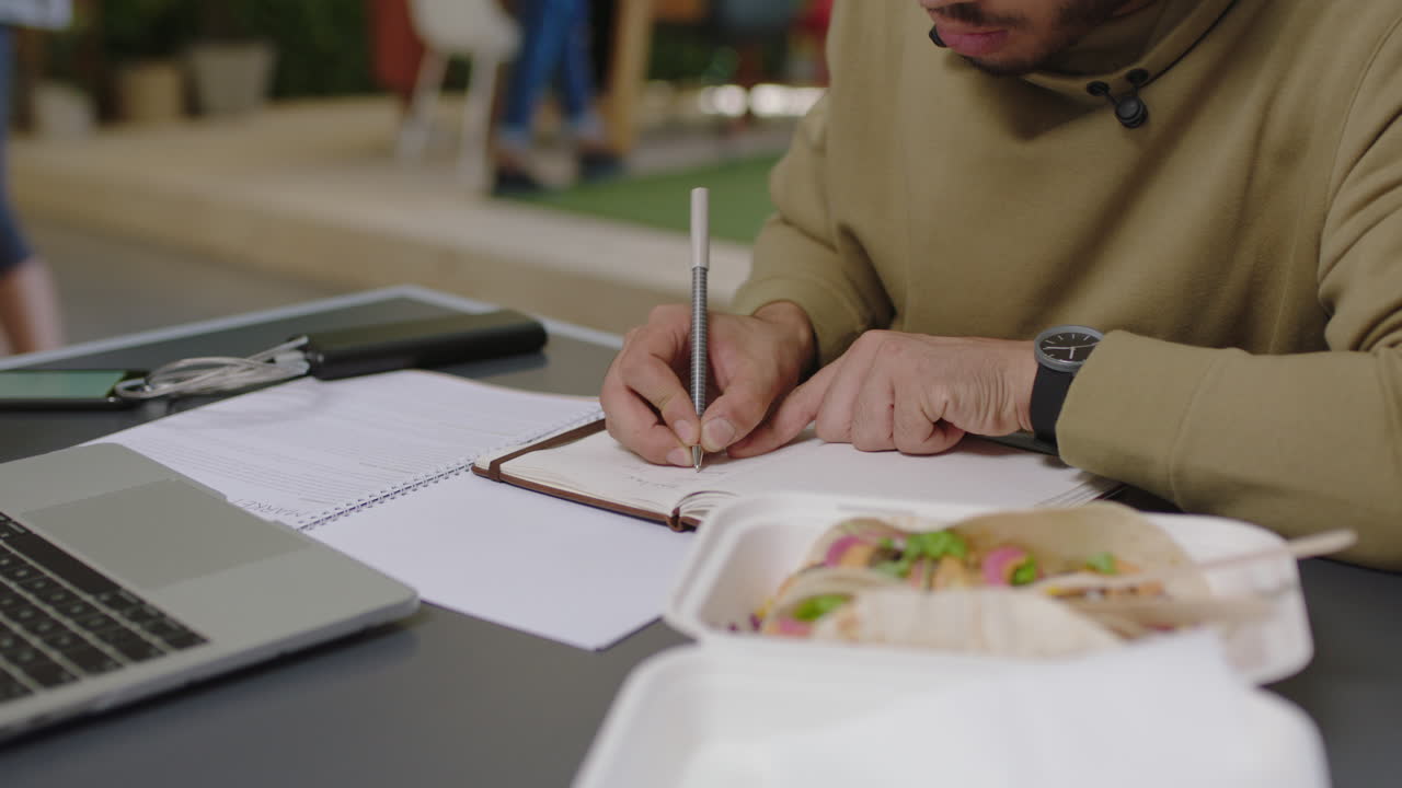young arab businessman student brainstorming writing notes enjoying study using laptop researching online listening to music in busy office workplace close up