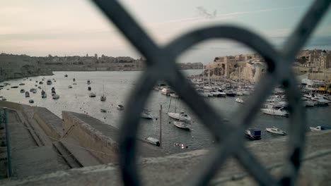 camera passes behind old fence showing the beautiful harbour of malta