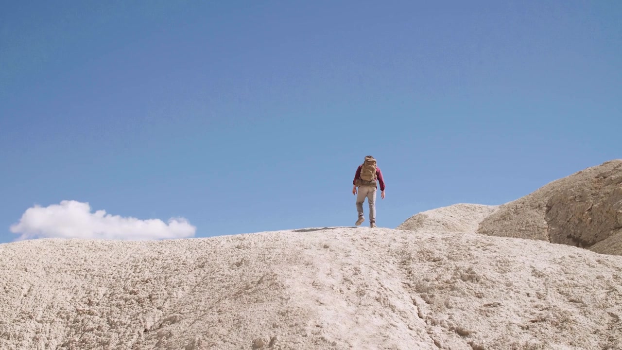 Caminhante com Mochila Subindo uma Colina Arenosa no Deserto